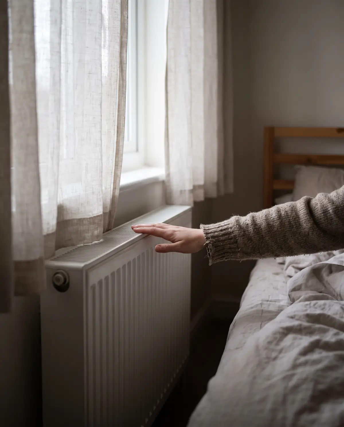 A hand resting on a warm radiator under a bedroom window