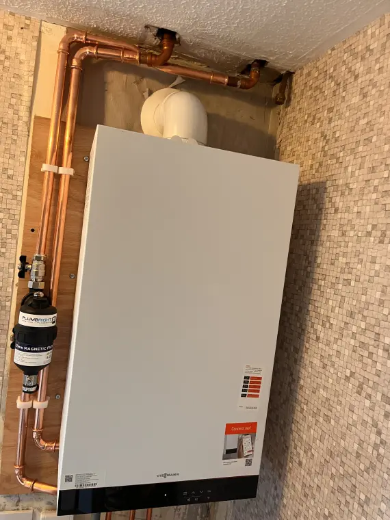 A wall-mounted boiler set against a mosaic tile splashback, with copper pipework and an expansion vessel.